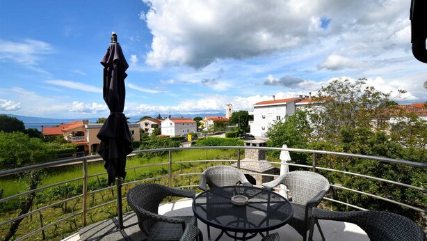 A balcony with wicker furniture and a table, overlooking a town with buildings and a church. - Apartment Luka 2 with Balcony (Malinska)