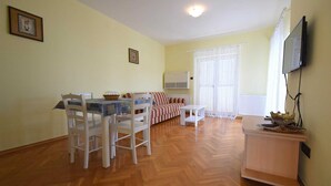 A living room with a dining area, a sofa, a TV mounted on the wall, and a radiator. - Apartment Luka 2 with Balcony (Malinska)