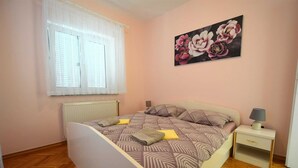 A bedroom with a bed, a nightstand, a lamp, a window with curtains, and a floral painting on the wall. - Apartment Luka 2 with Balcony (Malinska)