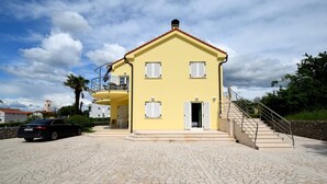 A yellow building with a balcony, a staircase, and a car parked in front. - Apartment Luka 2 with Balcony (Malinska)
