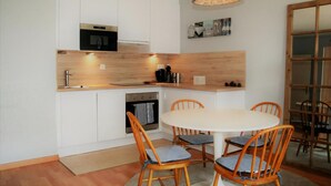 Una cocina compacta con armarios blancos, horno integrado y un comedor con mesa redonda y sillas de madera.