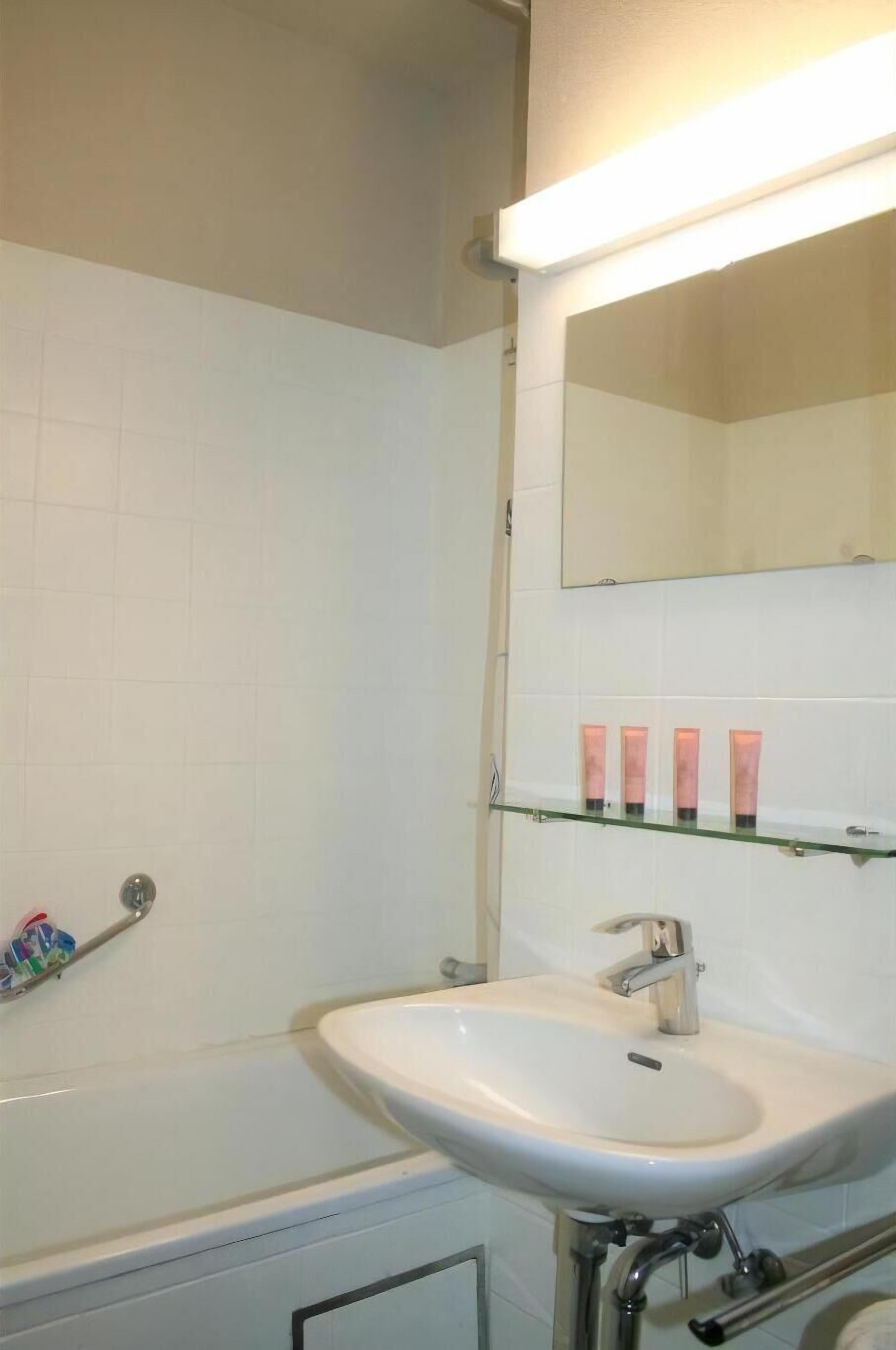 A bathroom with a white sink, a mirror, and a glass shelf with toiletries.