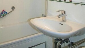 Un baño con un lavamanos blanco, un espejo y una repisa de vidrio con artículos de tocador.