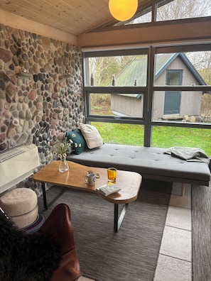 A cozy room with a stone wall, a large window, a bench, a wooden table, and a view of the outside.