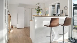 Una cocina moderna con una isla blanca, dos taburetes de bar, un refrigerador y una ventana con vistas.