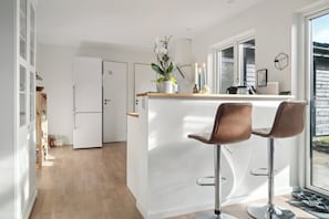A modern kitchen with a white island, two bar stools, a refrigerator, and a window with a view.