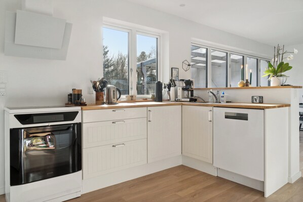 Een moderne keuken met witte kasten, een inbouwoven, een vaatwasser en een houten aanrecht.