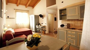 A hotel room with a bed, a dining table with a vase of flowers, a kitchen area with cabinets and a microwave, and a small seating area with a chair. - STUDIO APARTMENT A FEW KM FROM THE BEACH OF CESENATICO (cesenatico)