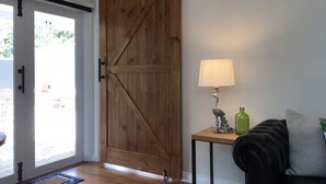 Une porte en bois de style grange, une petite table avec une lampe et un canapé en cuir noir.