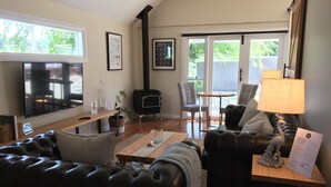 Un salon avec un canapé en cuir noir, une table basse en bois, une cheminée, un téléviseur et une grande fenêtre.