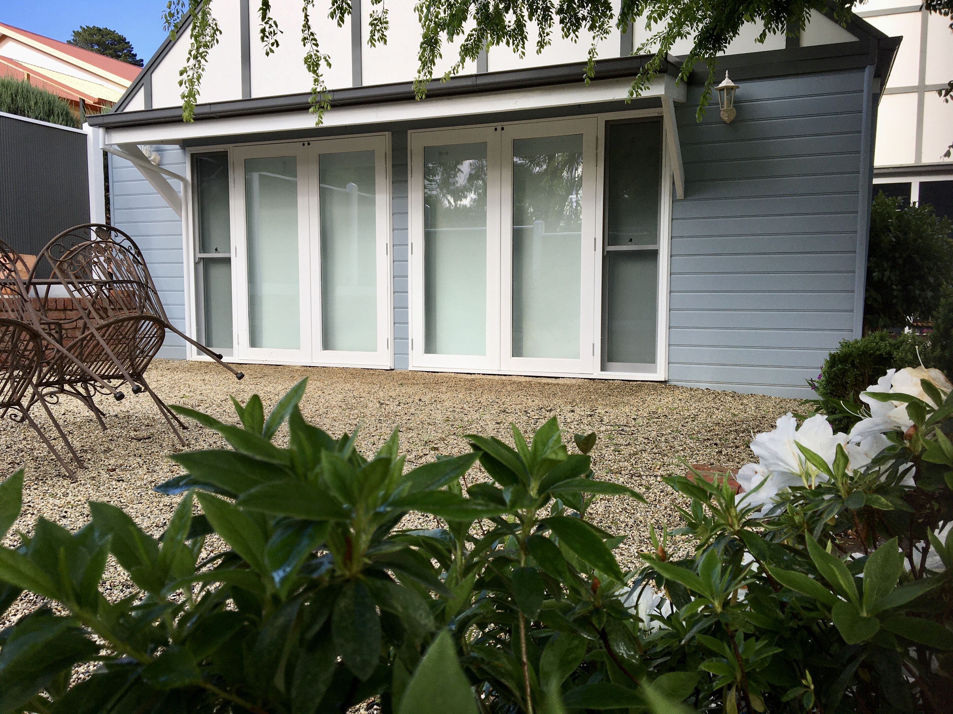 A house with a covered patio area, a metal chair, and a gravel driveway.