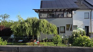 En toetages bygning med solpaneler på taget, en indhegnet have og en klar blå himmel.