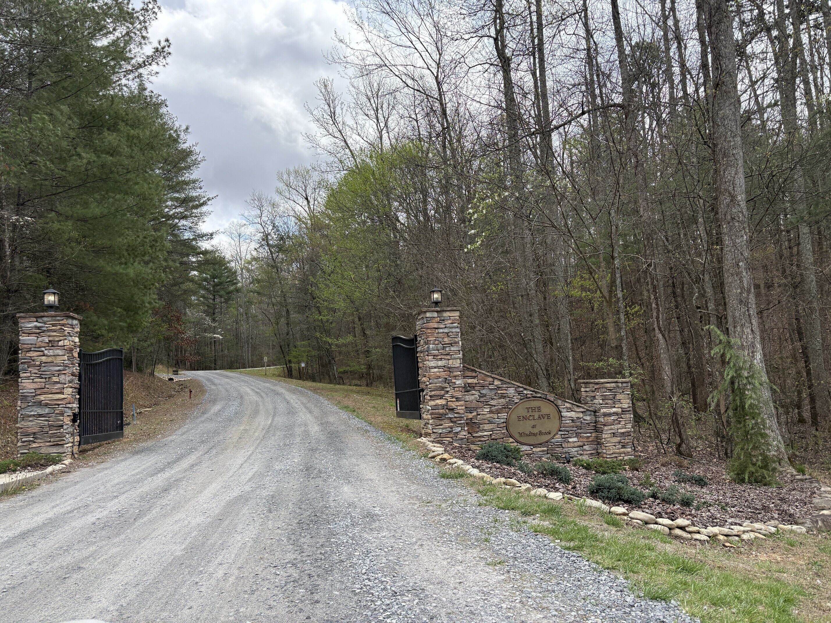 Un camino de grava conduce a una puerta de piedra con un cartel que dice 'The Enclave at Winding Brook'.