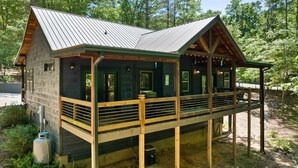 Een chalet met een overdekte veranda, houten terras en een metalen dak.