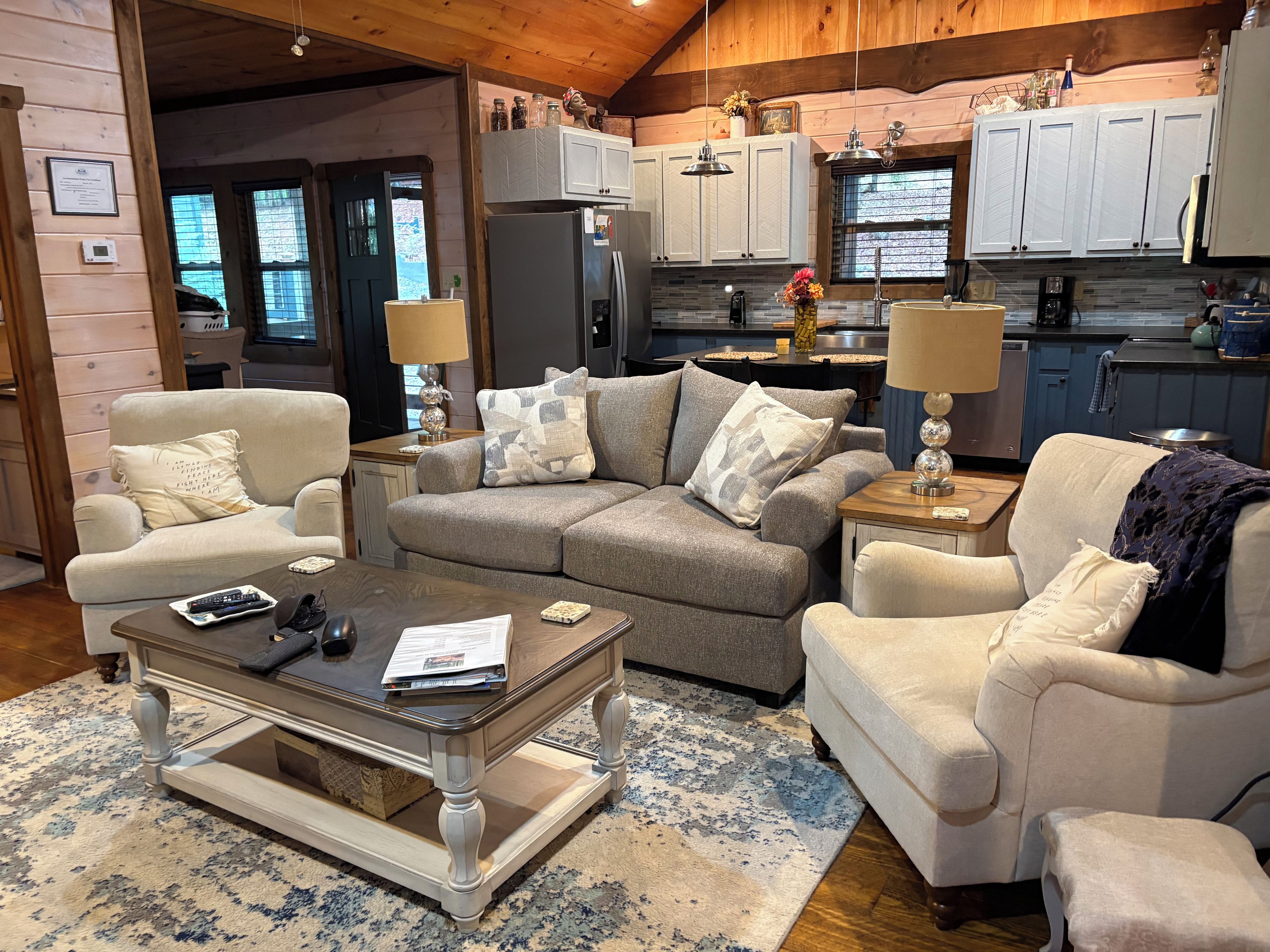 A cozy living room with a sofa, armchairs, a coffee table, and a kitchen in the background.
