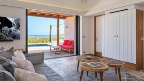 A modern living room with a large window overlooking a pool and ocean, a red sofa, a wooden coffee table, and a white wardrobe.
