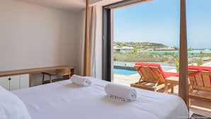 Ein Hotelzimmer mit großem Fenster, einem Bett mit zwei zusammengerollten Handtüchern, einer hölzernen Bank und Blick auf Pool und Resort.