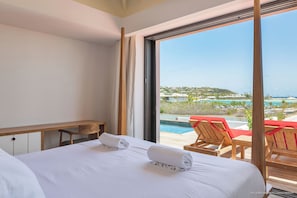 Une chambre d’hôtel dotée d’une grande fenêtre, d’un lit avec deux serviettes roulées, d’un banc en bois et offrant une vue sur une piscine et un espace de loisirs.