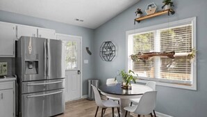 Une cuisine moderne équipée d’appareils électroménagers en acier inoxydable, une table à manger avec des chaises et une fenêtre avec des stores.