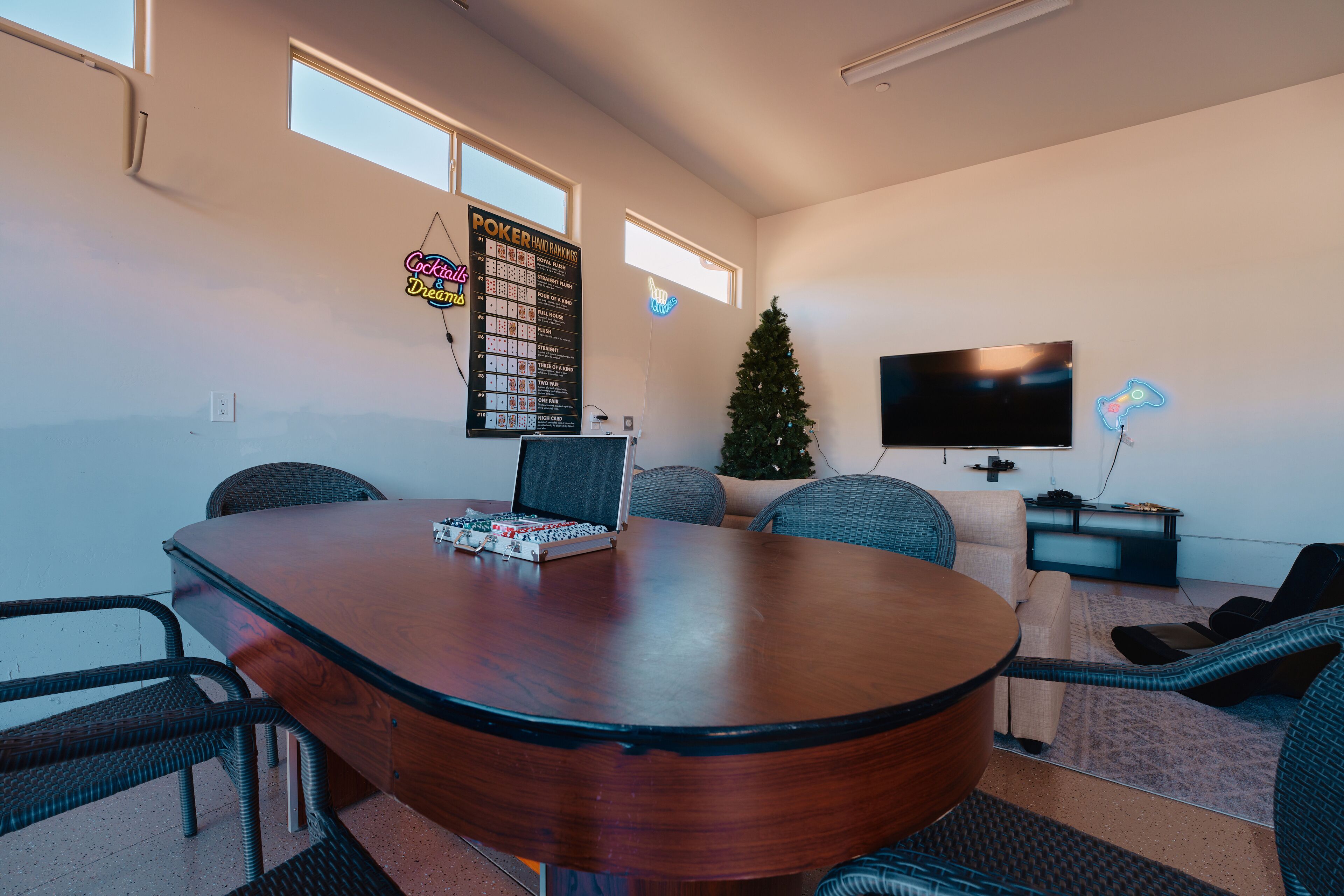 Un salón de conferencias con una gran mesa de madera, sillas de mimbre, un árbol de Navidad, un letrero de neón, un televisor y un cartel con una mano de póker.