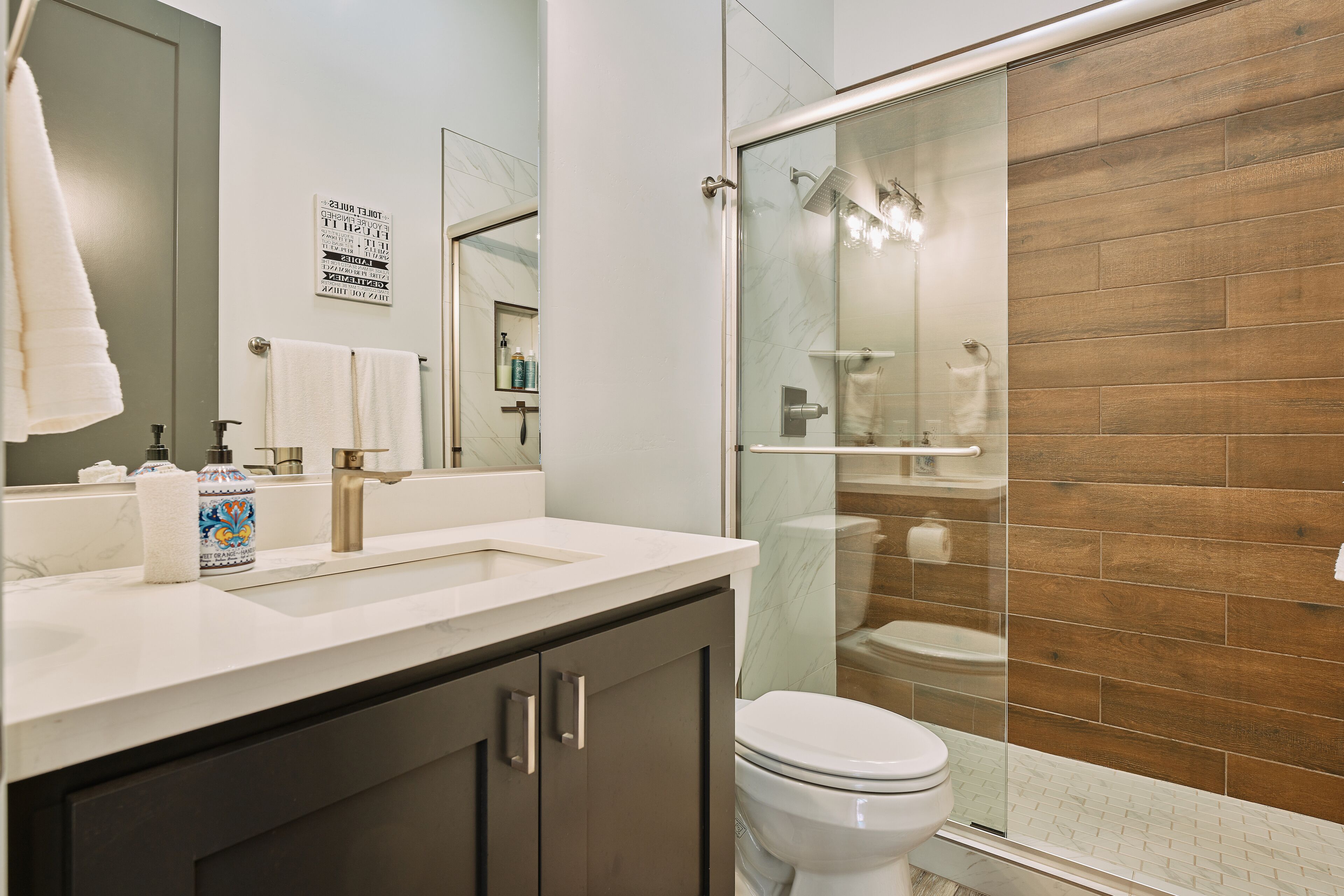 Une salle de bain moderne avec une douche à parois de verre, des toilettes et un lavabo surmonté d’un miroir.
