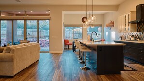 A modern kitchen with a central island, bar stools, and a dining area with a sofa and chairs. - New Build in Heart of Sedona (Sedona)