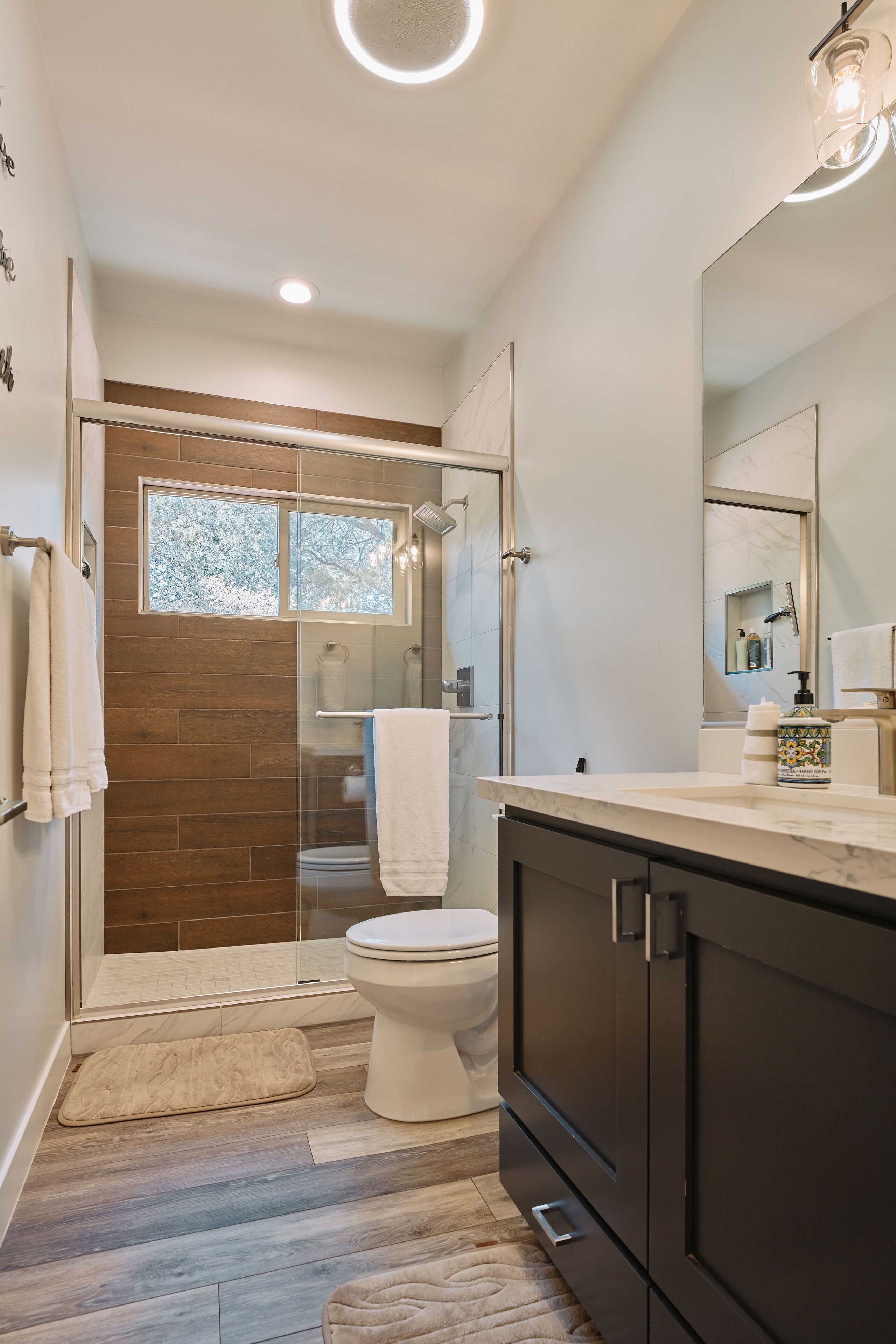 A modern bathroom with a glass-enclosed shower, a white toilet, and a dark wooden cabinet.