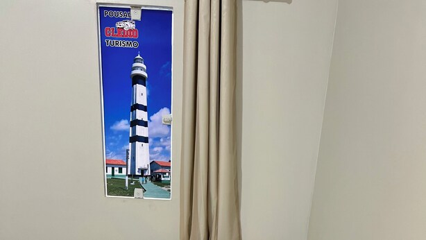 A hotel room with a bed, beige curtains, a poster of a lighthouse, and towels with a tag. - Pousada e agência cledio turismo  (Barreirinhas)