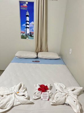 A hotel room with a bed, beige curtains, a poster of a lighthouse, and towels with a tag. - Pousada e agência cledio turismo  (Barreirinhas)