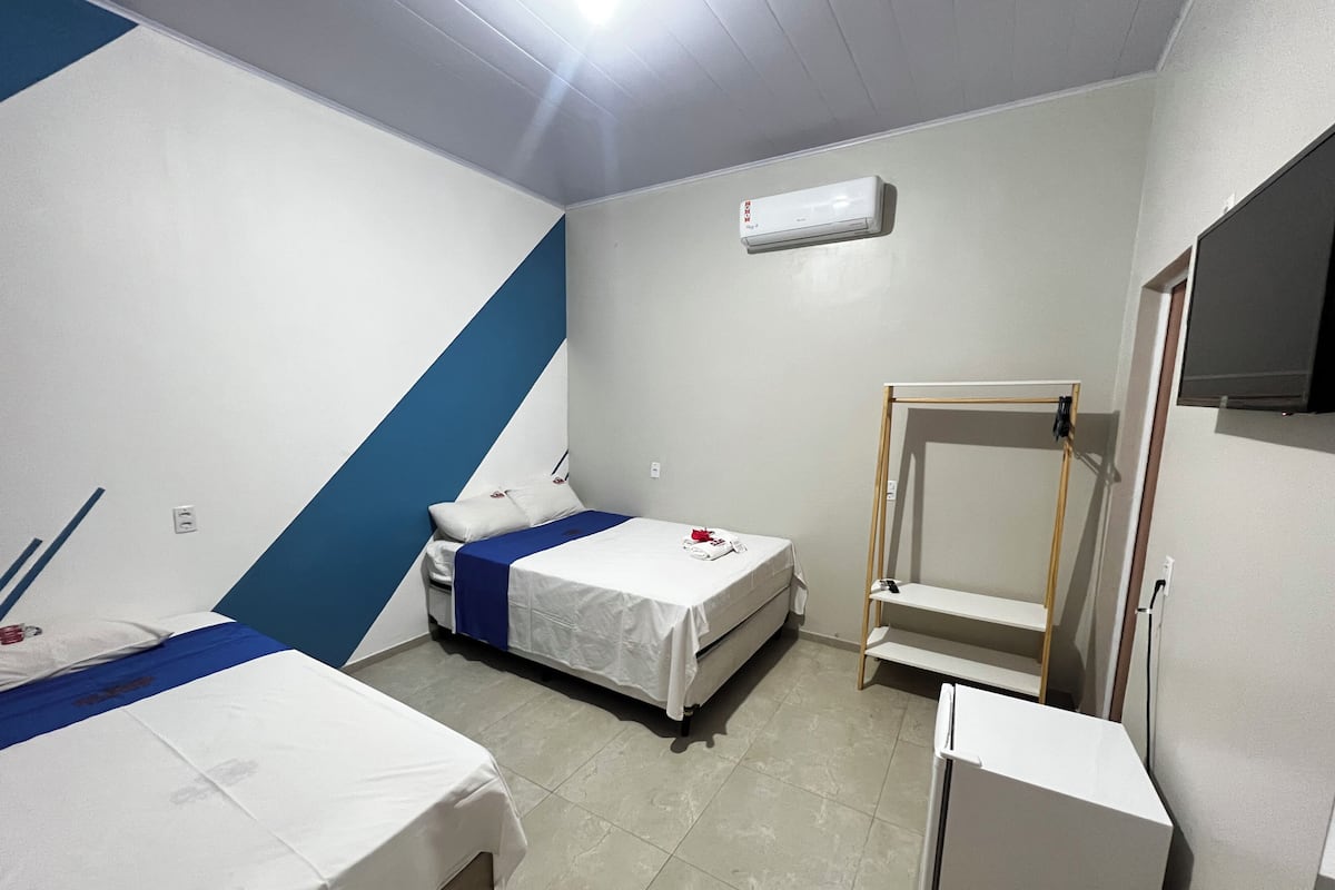 A hotel room with two beds, a small desk, a wardrobe, and a ceiling fan.