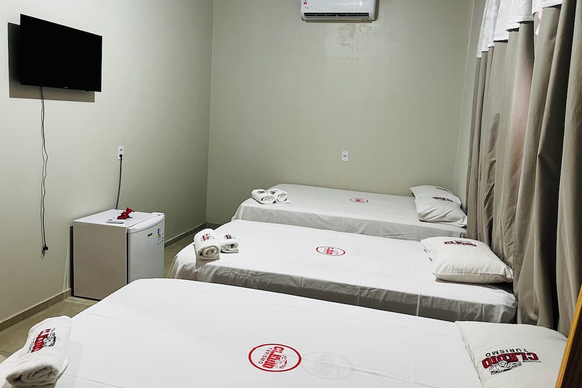 A small hotel room with two single beds, a TV mounted on the wall, an air conditioner, and a small table with a red object on it.