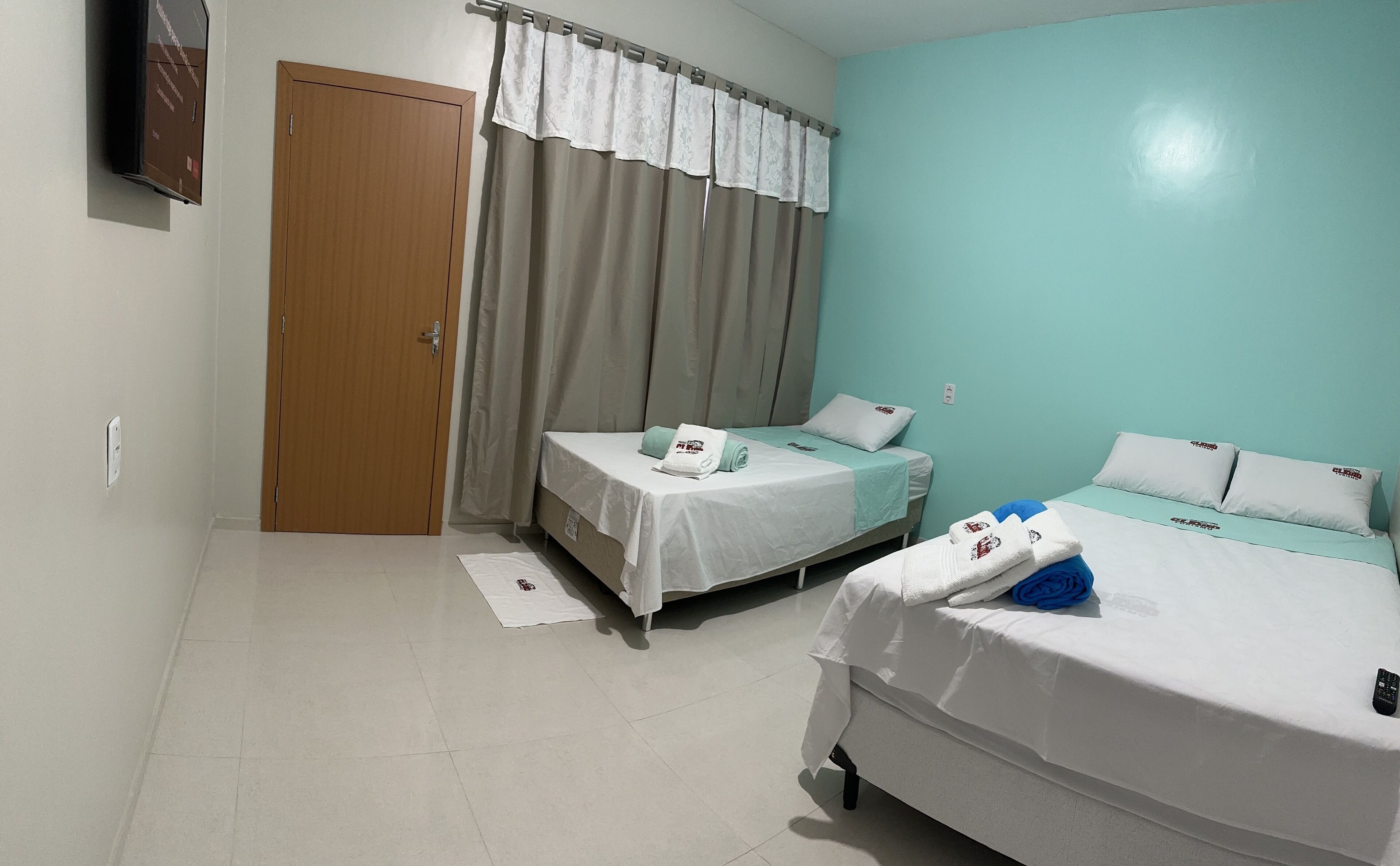 A hotel room with two beds, a wooden door, a window with curtains, and a teal wall.