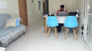 A modern living room with a sofa, a dining table with two chairs, and a person working on a laptop. - Pousada e agência cledio turismo  (Barreirinhas)
