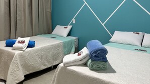 A hotel room with two beds, each with a white quilted bedspread and matching pillows. There are towels and a folded blanket on the beds. The room has a teal accent wall with a geometric pattern and a window with curtains. - Pousada e agência cledio turismo  (Barreirinhas)