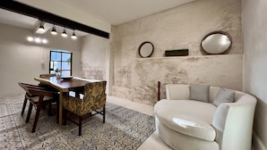 Un soggiorno moderno con zona pranzo, caratterizzato da una parete in marmo, uno specchio rotondo, un divano con cuscini decorati e un tappeto a motivi.