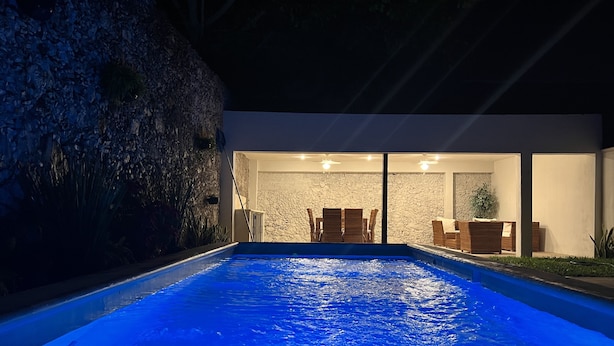 Area piscina esterna moderna con muro in pietra e zona relax.