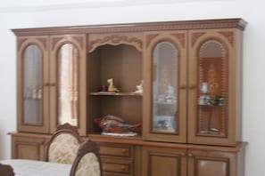A wooden cabinet with glass doors, a chair, and a small shelf with decorative items.