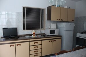 A kitchen with a microwave, refrigerator, stove, and a window with blinds.