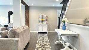 Ein modernes Wohnzimmer mit einem länglichen, gemusterten Teppich, einer Couch, einer weißen Kommode mit dekorativen Spiegeln und einer Treppe mit einer blauen Vase auf der Zwischenebene.