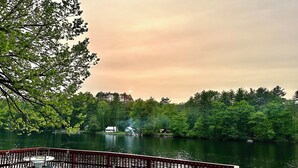 Eine Holzterrasse mit Gartenmöbeln mit Blick auf einen See, umgeben von Bäumen und einem Sonnenuntergangshimmel.