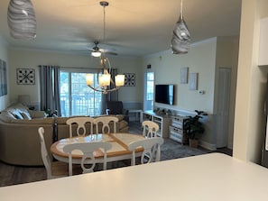Ein modernes Wohnzimmer mit Essbereich, Deckenventilator, Fernseher und einem großen Fenster.