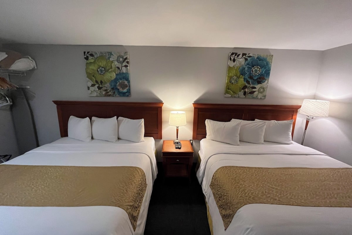 Habitación de hotel con dos camas, cada una con ropa blanca y una manta marrón. Hay dos mesitas de noche con lámparas, y las paredes están decoradas con motivos florales.