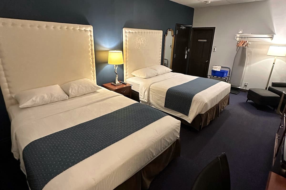 Habitación de hotel con dos camas, un escritorio, una silla, un espejo y un armario.