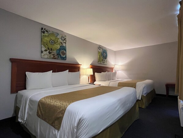Habitación de hotel con dos camas, cabecero de madera, ropa de cama blanca, manta marrón, mesita de noche con lámpara y obras de arte florales en las paredes.