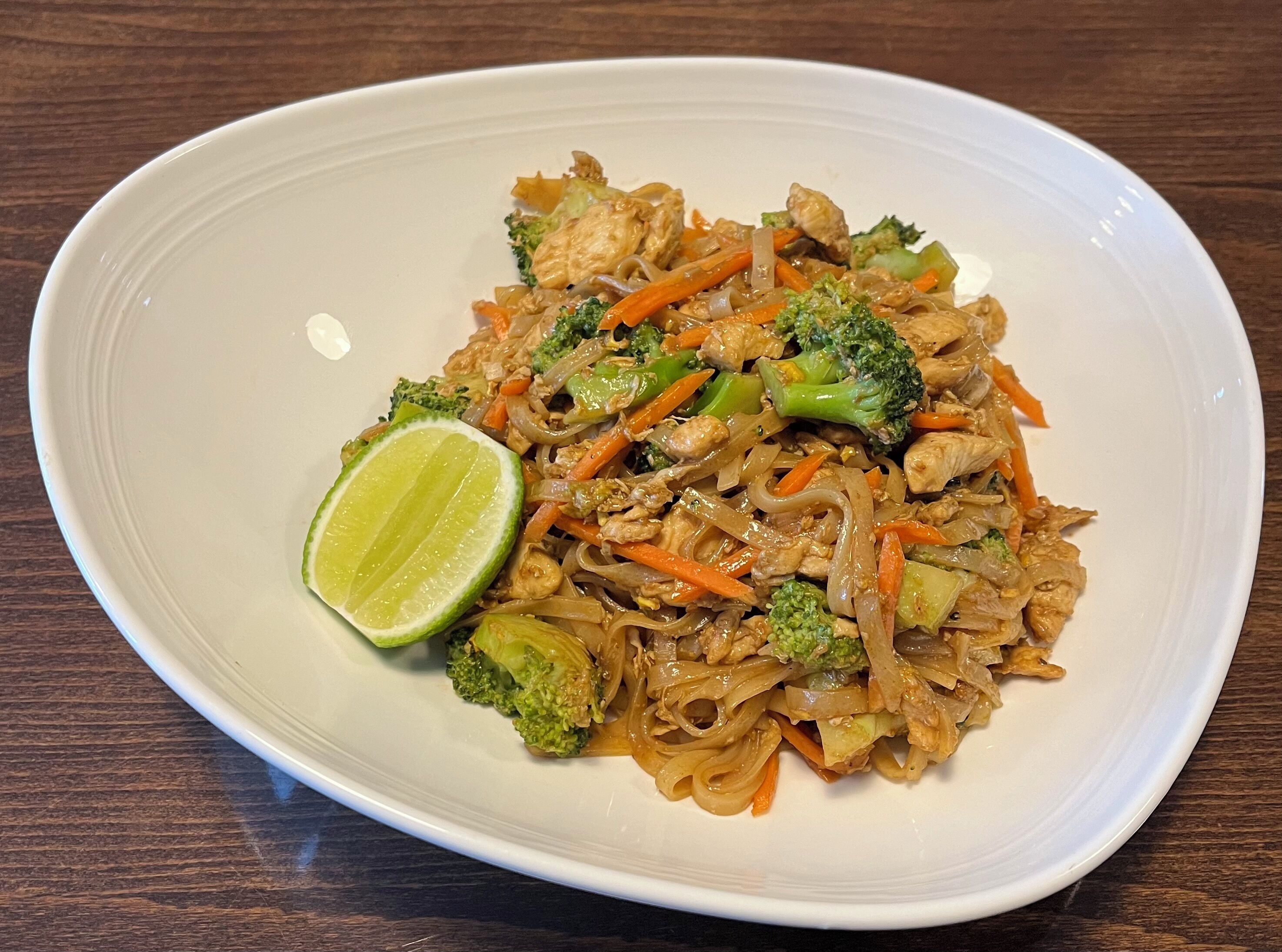 Un plato de fideos salteados con vegetales y pollo, adornado con una rodaja de lima.