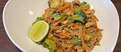 Un plato de fideos salteados con vegetales y pollo, adornado con una rodaja de lima.