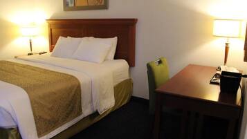 A hotel room with a bed, two bedside lamps, a wooden headboard, a green chair, and a small table with a lamp.