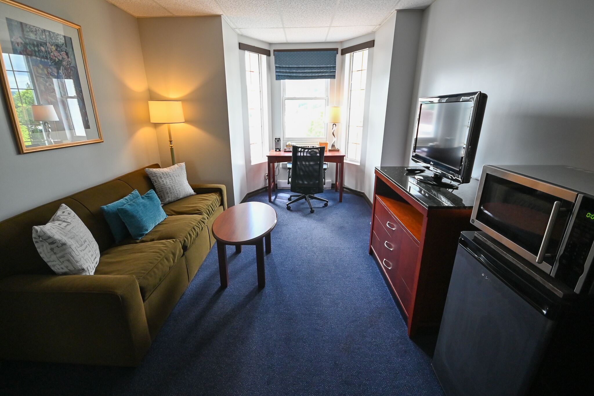 A compact hotel room with a sofa, a small table, a desk with a chair, a television, and a microwave.
