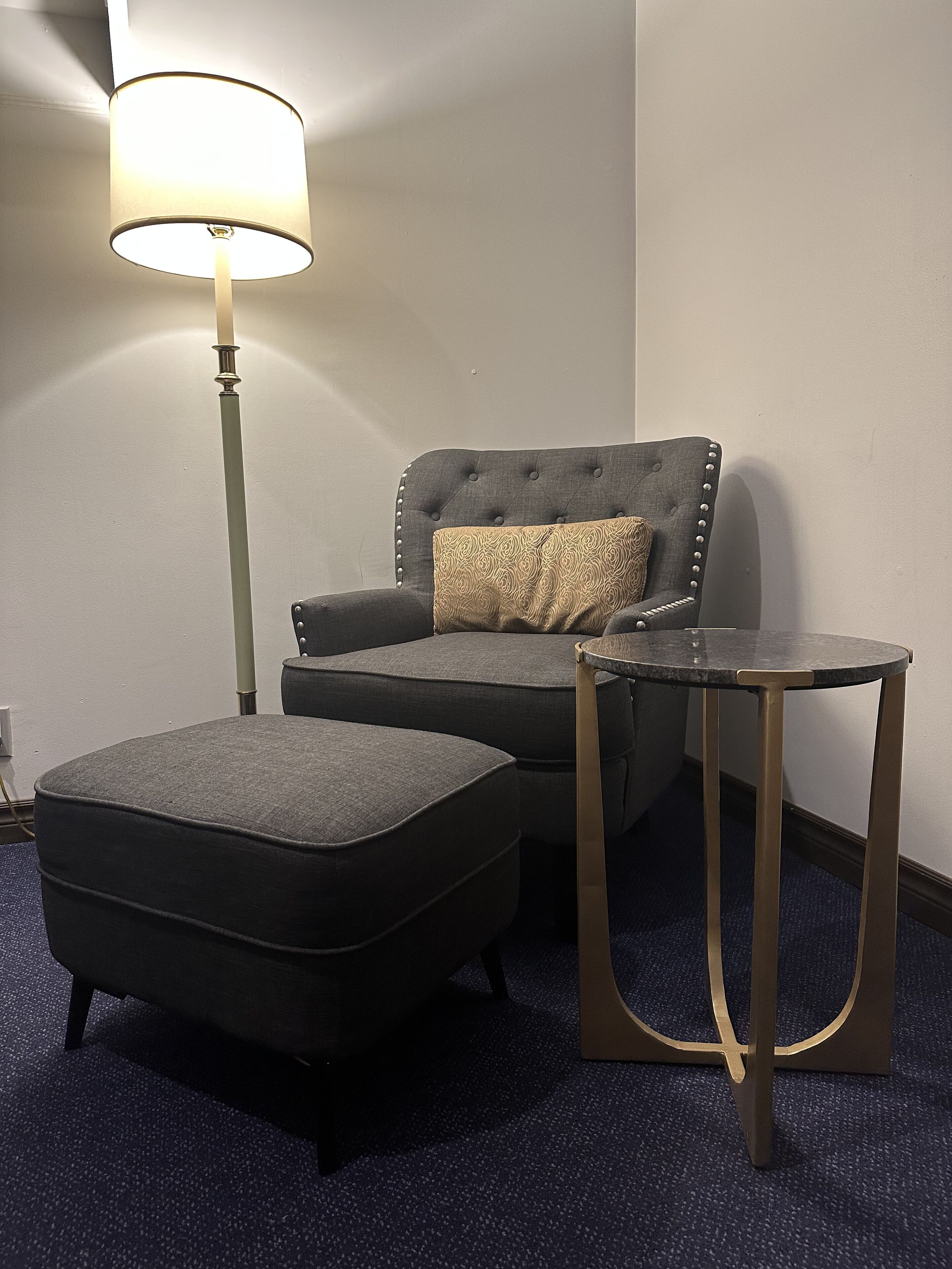 Una habitación con un sillón capitoné, un reposapiés a juego y una mesita de noche con una lámpara.