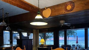 Ein gemütlicher Essbereich mit Holztisch und Stühlen, einer Hängeleuchte und Blick auf das Meer durch große Fenster.